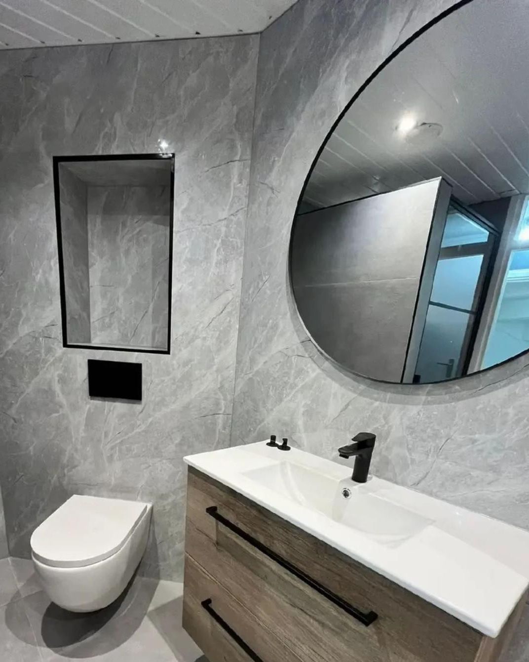 Badkamer in grijze marmerlook met hangend toilet, wastafelmeubel en ronde spiegel