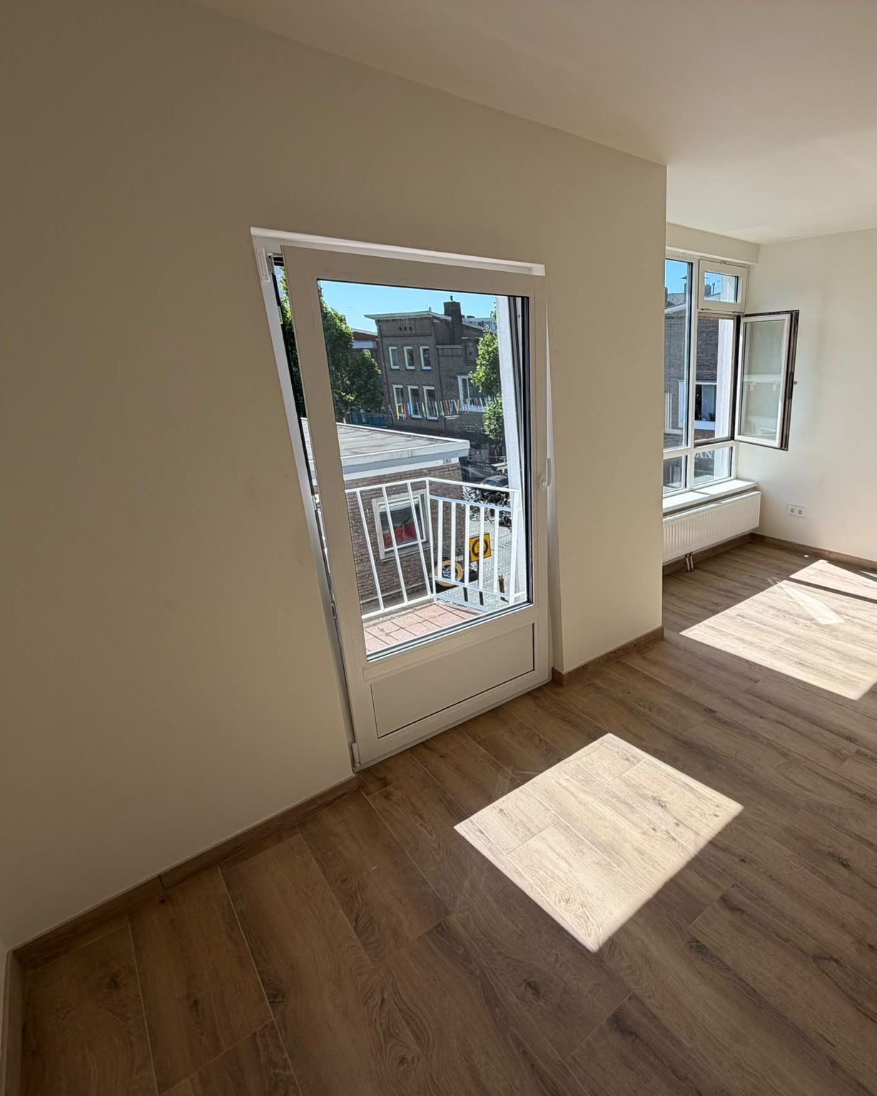 Gerenoveerde kamer met strak afgewerkte witte wanden, houtlook vloer en balkondeur