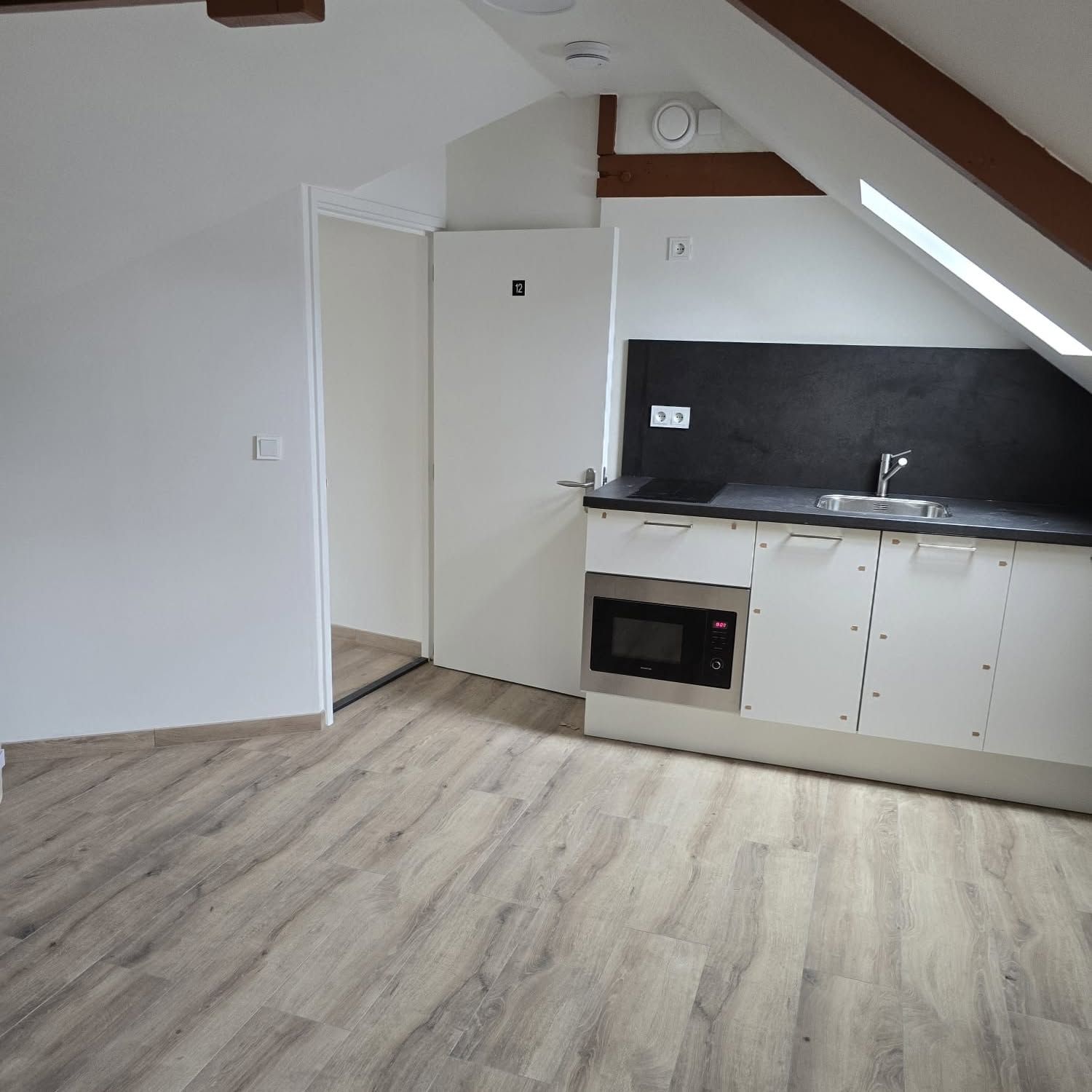 Zolderstudio onder een schuin dak met keukenblok en houtlook vloer