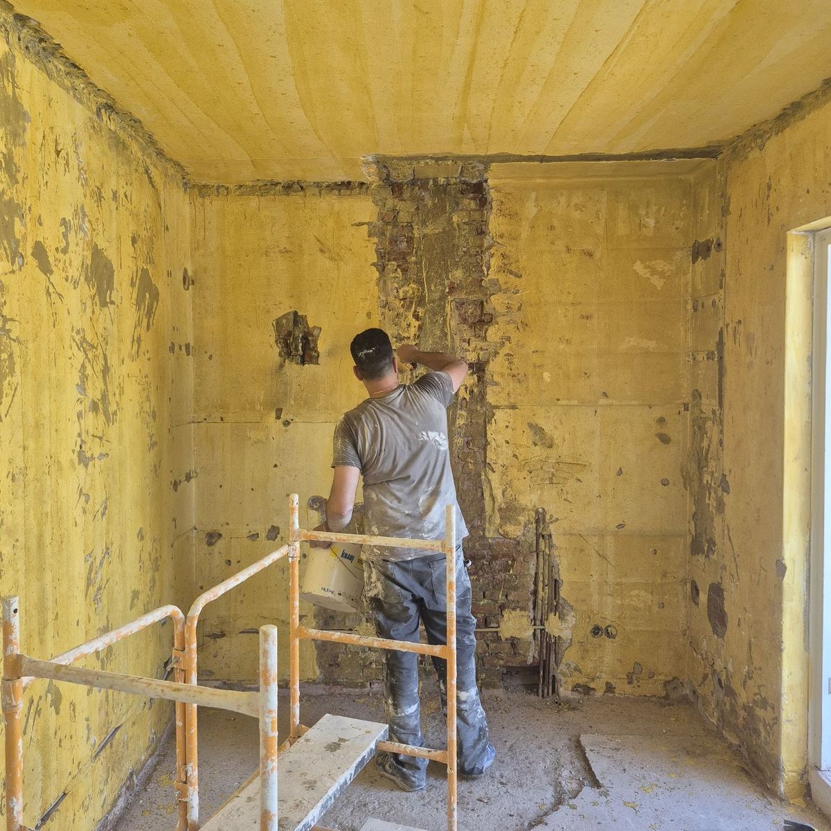 Vakman van Boka aan het werk op een steiger in een kamer die wordt verbouwd