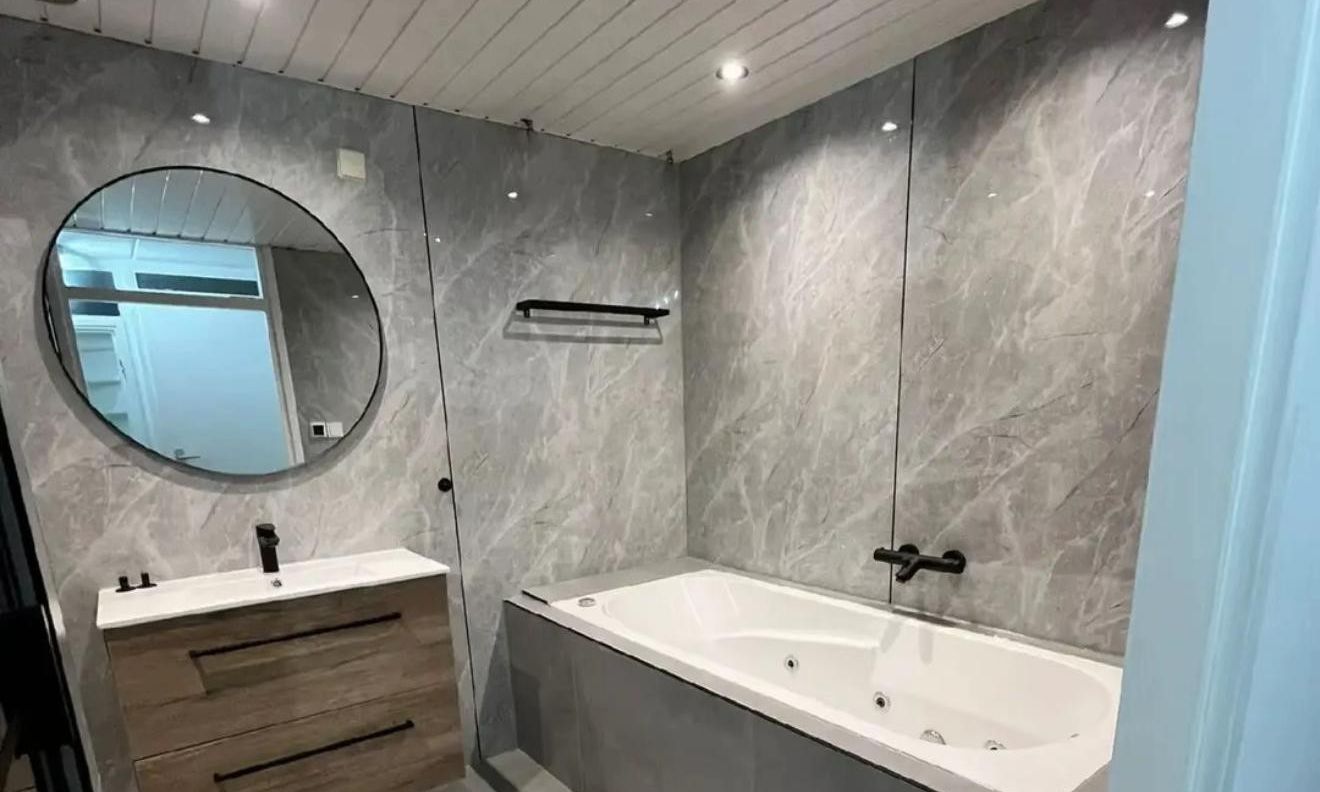 Badkamer in grijze marmerlook met whirlpoolbad, wastafelmeubel en ronde spiegel