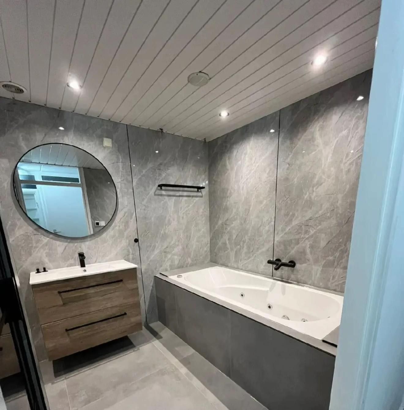 Badkamer in grijze marmerlook met whirlpoolbad, wastafelmeubel en ronde spiegel